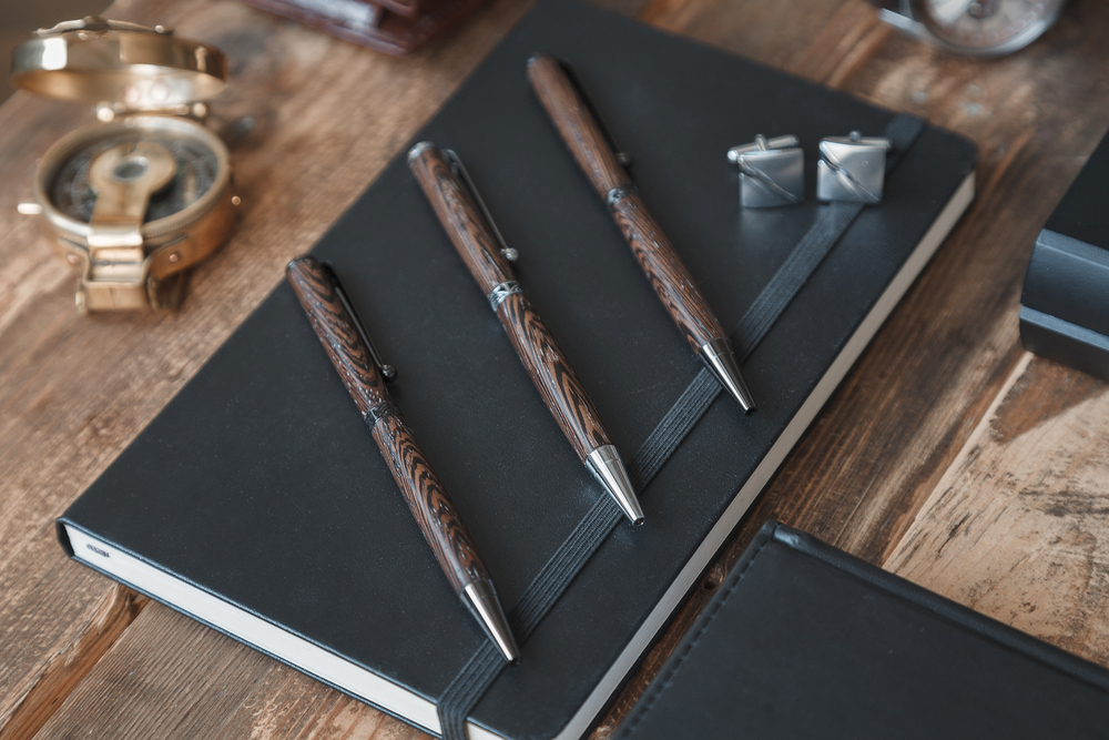 scrivania in legno con agenda nera e penne in radica